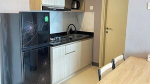 A compact kitchen with a black refrigerator, a sink, and a stove. There is a wooden dining table and a door to the right. - 2 BR ANDERSON 25floor above pakuwon mall the biggest shopping center (Wiyung)
