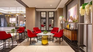 A modern lobby with a round table surrounded by red chairs, a reception desk, and a large window with a view of the interior. - 2 BR ANDERSON 25floor above pakuwon mall the biggest shopping center (Wiyung)