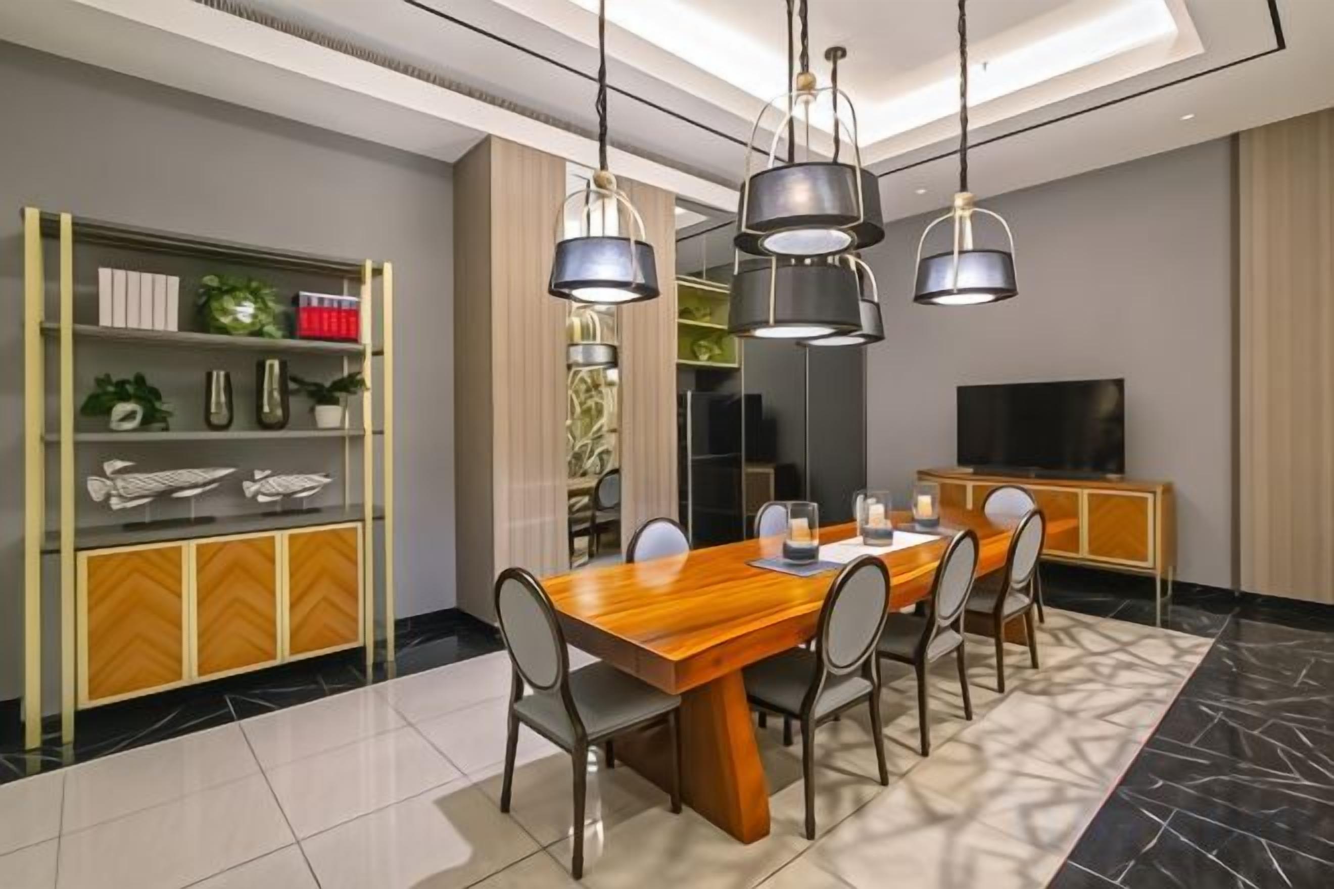 A modern dining area with a wooden table, chairs, pendant lights, and a television on a cabinet.