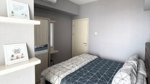 A bedroom with a bed, a door, and a shelf with framed pictures. - 2 BR ANDERSON 25floor above pakuwon mall the biggest shopping center (Wiyung)