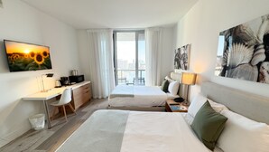 Camera d'albergo con due letti, una scrivania, una sedia, una televisione e vista sulla città.
