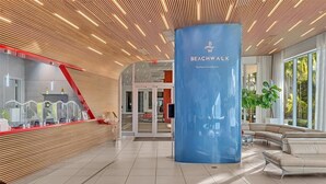 Una hall moderna con una reception, un pilastro blu con la scritta 'Beachwalk' e un'area relax con vista sull'esterno.