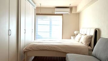 Un dormitorio con cama, mesita de noche, lámpara, armario y ventana.