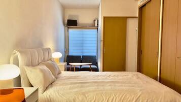 A hotel room with a bed, bedside table, lamp, and a view of a balcony.