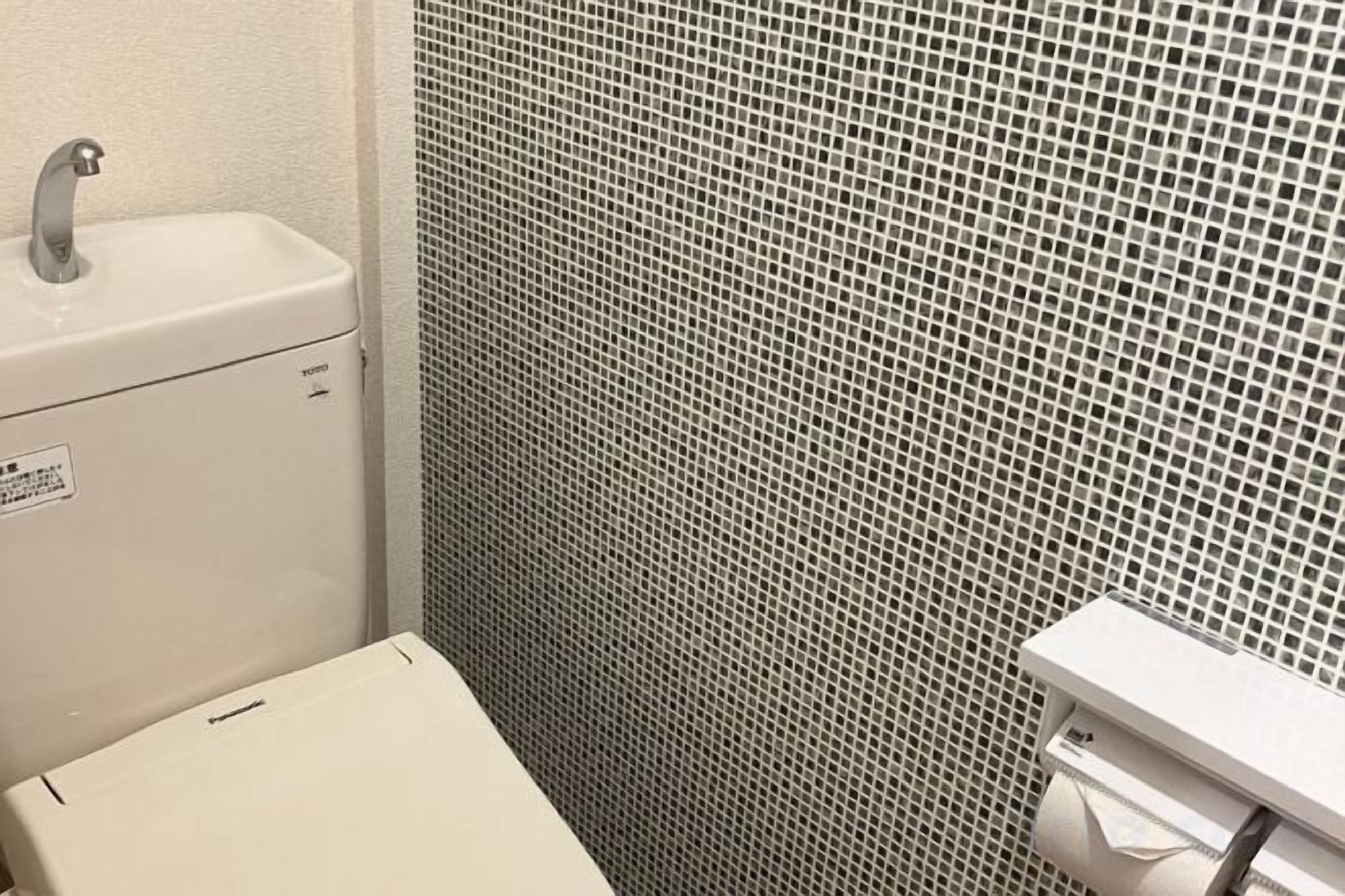 A bathroom with a toilet, a sink, and a tiled shower wall.
