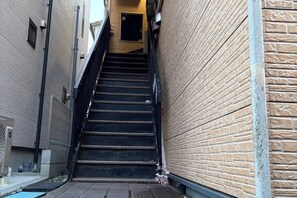 A narrow stairway leading to an upper level, flanked by brick walls, with a door at the top. - CUBE STAY KITA-TOKYO (Tokyo)