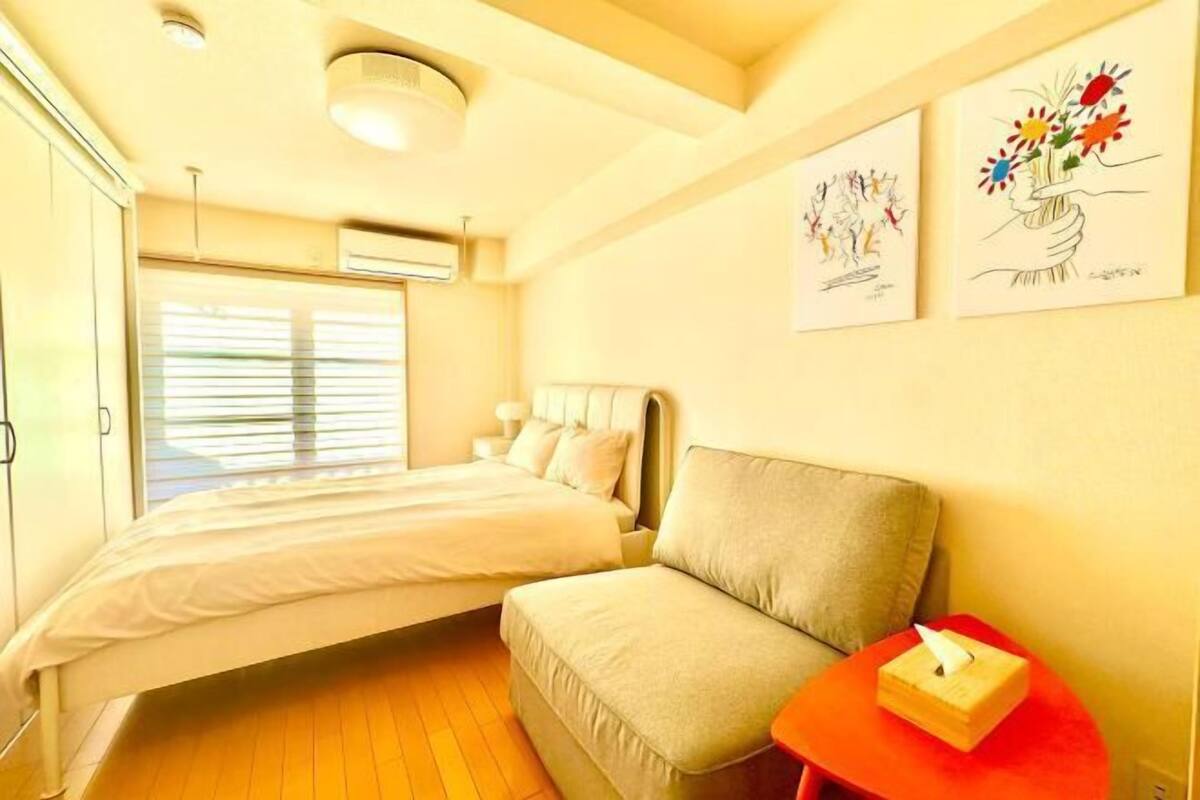 A bedroom with a bed, a sofa, a bedside table with a tissue box, and two wall-mounted artworks.