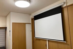 A room with a white projection screen, wooden doors, and a ceiling light. - CUBE STAY KITA-TOKYO (Tokyo)