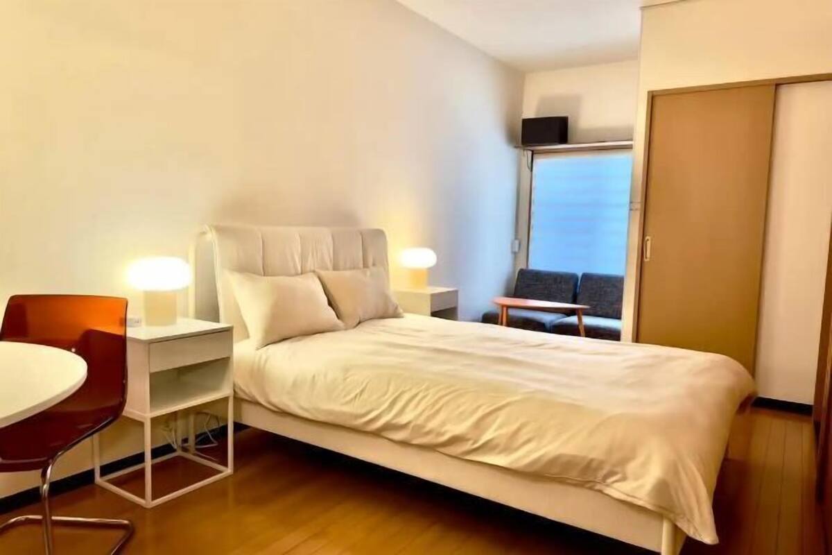 A hotel room with a bed, a desk with a chair, a small table, and a window with a view.