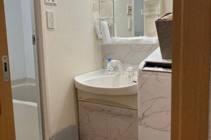 A bathroom with a white sink, marble-patterned cabinets, a mirror, and a towel dispenser. - CUBE STAY KITA-TOKYO (Tokyo)