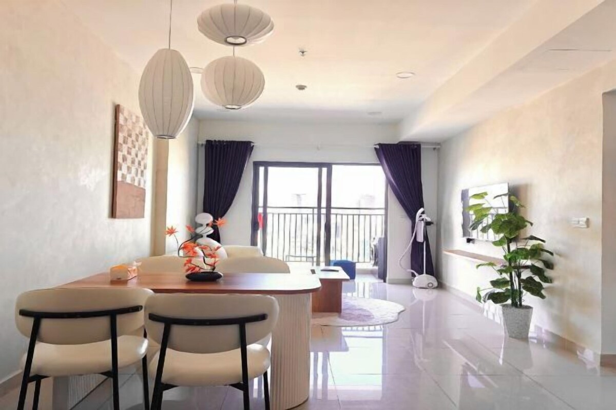 A modern living room with a dining table, chairs, a TV, and a potted plant.