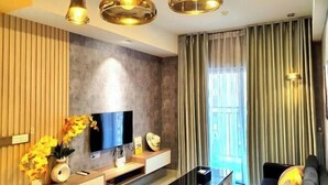 A modern living room with a flat-screen TV, wooden panel wall, and a large window with curtains. - Soho Residence-Tony Apartment (Ho Chi Minh City)