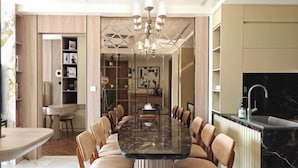 A modern dining area with a long table and chairs, a kitchen with a black countertop, and a chandelier. - Soho Residence-Tony Apartment (Ho Chi Minh City)