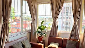 A room with a sofa set, a potted plant, and large windows with curtains. - Deepjyoti Inn (Kathmandu)