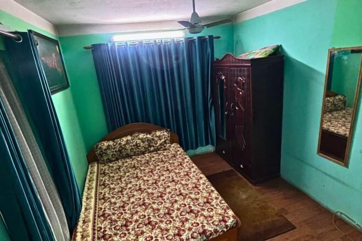 A bedroom with a bed, a wardrobe, a ceiling fan, and a mirror on the wall.