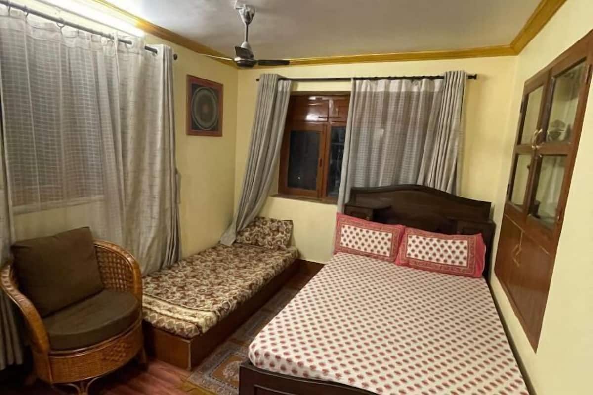 A single room with a bed, a chair, a small table, and a window with curtains.