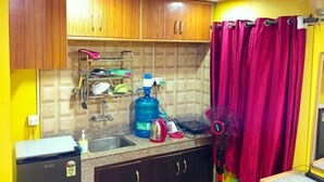 A kitchen with wooden cabinets, a sink, a gas stove, and a red curtain. - Deepjyoti Inn (Kathmandu)
