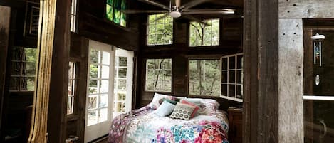 Une chambre à coucher rustique, avec un lit, un ventilateur de plafond et de grandes fenêtres.