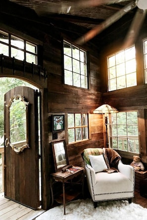 Une cabane rustique avec un intérieur en bois, une grande fenêtre, une chaise et une lampe.