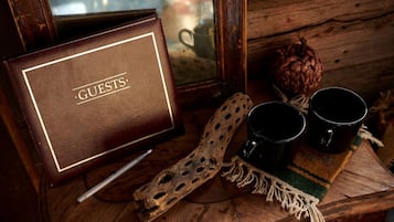 Une table en bois sur laquelle repose une plaque en cuir portant l’inscription « CLIENTS », deux tasses noires, une cuillère en bois sculptée et un set de table tissé.