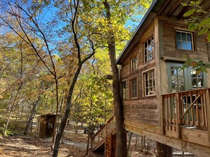 A wooden cabin with a deck, surrounded by trees with autumn foliage.
