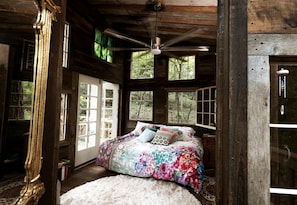 Une chambre à coucher rustique, avec un lit, un ventilateur de plafond et de grandes fenêtres.