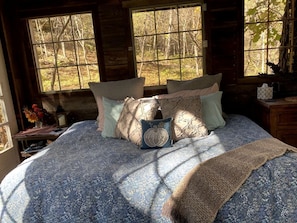 Un lit avec une literie à motifs, des oreillers et une couverture, dans une pièce aux murs en bois et aux grandes fenêtres.