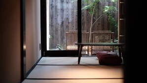 A traditional Japanese room with tatami flooring, a sliding door leading to an outdoor area with a wooden fence and a table with cushions. - Kyokoi Kiyomizu Gojo (Kyoto)