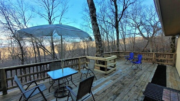 A wooden deck with a table and chairs, a covered area, and a view of trees and hills.