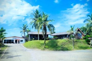 A building with a sloped roof, surrounded by palm trees and a clear sky. - Marang Guesthouse Resort (Rusila)