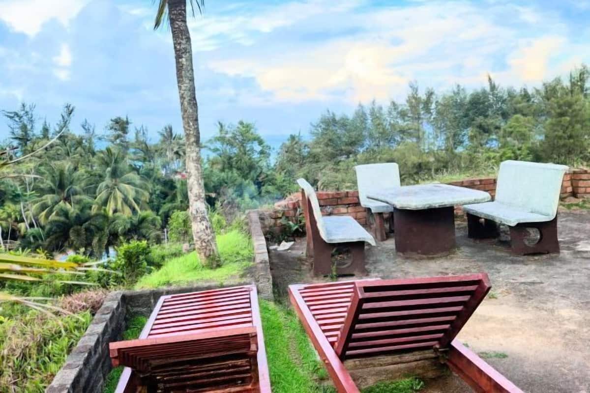 An outdoor seating area with benches and a table, surrounded by lush greenery and a view of the landscape.