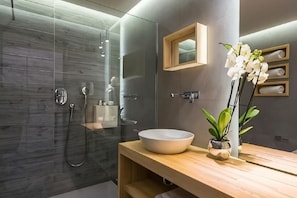 A modern bathroom with a glass shower enclosure, a wooden vanity, a white basin, and a potted orchid. - Arkadia Hotel (Arkadii)