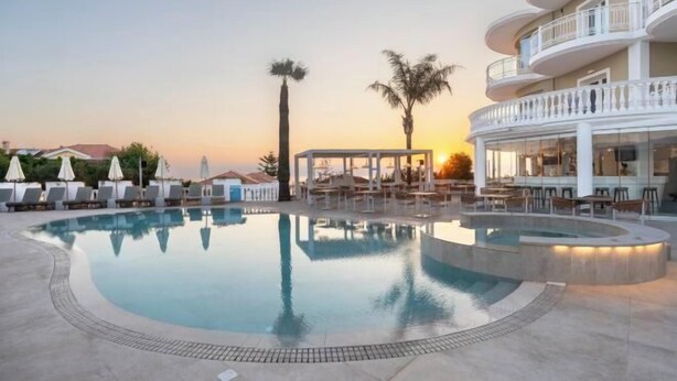 A swimming pool with lounge chairs, a covered seating area, and a building with balconies. - Arkadia Hotel (Arkadii)
