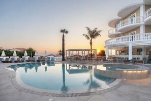 A swimming pool with lounge chairs, a covered seating area, and a building with balconies. - Arkadia Hotel (Arkadii)