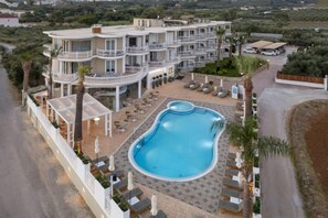 Et hotel med flere etager, en swimmingpool, udendørs siddepladser og en anlagt have.