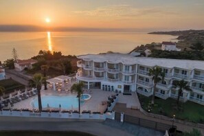 Un hotel con piscina, diversi balconi e vista mare al tramonto.