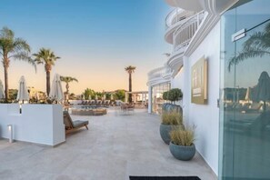 Una terrazza panoramica con posti a sedere all'aperto, palme e una moderna facciata dell'edificio.