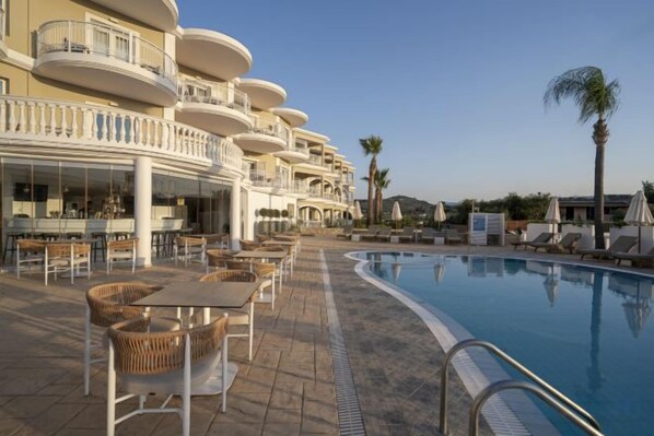 A poolside area with lounge chairs and tables, a swimming pool, and a building with balconies.