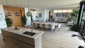 A modern kitchen with a central island, dining area with round tables and chairs, and a living room with a sofa and decorative items.
