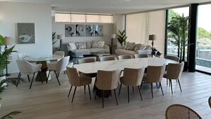 A modern living room with a large dining table, sofas, and a view of a cityscape through large windows.