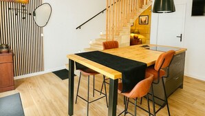 A modern kitchen with a wooden table and chairs, a black pendant light, and a staircase leading to an upper level.