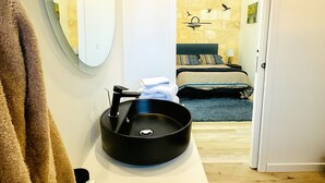 A bathroom with a round mirror, a black sink, and a towel rack.