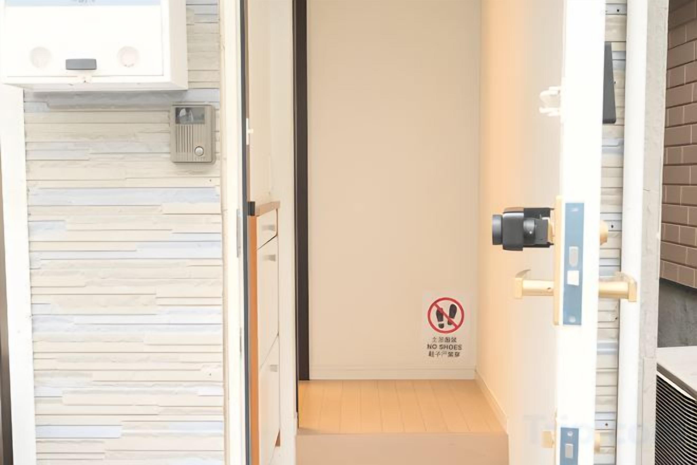 An interior view of a hotel room with a closed door, a wooden floor, and a wall-mounted intercom system.