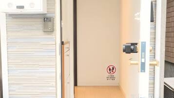 An interior view of a hotel room with a closed door, a wooden floor, and a wall-mounted intercom system.