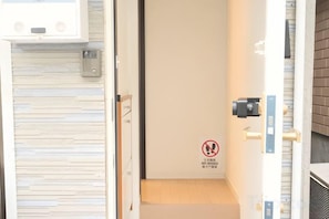 Blick in ein Hotelzimmer mit geschlossener Tür, Holzboden und einem an der Wand montierten Gegensprechanlage.