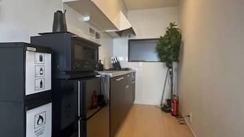A compact kitchen with a microwave, oven, and refrigerator. There is a plant and a fire extinguisher visible.