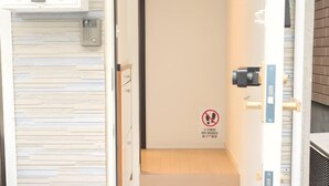 L'ingresso di una camera d'albergo con pavimento in legno, una porta con il cartello 'No Shoes' e una telecamera di sicurezza.