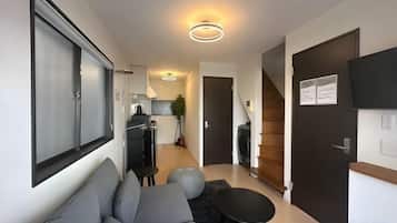 A modern living room with a sofa, a small round table, and a black rug. There is a kitchen area with a stove and cabinets in the background.