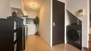 Un pasillo estrecho con una zona de cocina en un lado, una lavadora en el otro y una puerta que da a otra habitación.