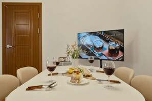 Et spisebord dækket med tallerkener, glas og bestik, en vase med blomster og et fjernsyn, der viser en reklame for en drik.